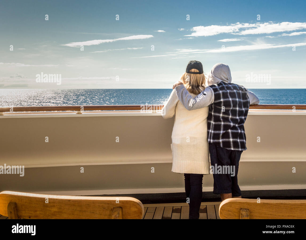 Casually dressed couple on Alaskan Inside Passage cruise looking out to open ocean from a sunlit exterior ship deck. Stock Photo