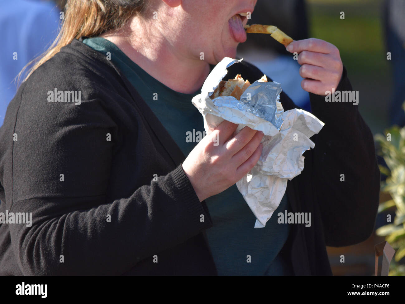 Obese lady eating fast food in the street in the UK where high streets have the highest concentration of fast food outlets in almost a decade Stock Photo