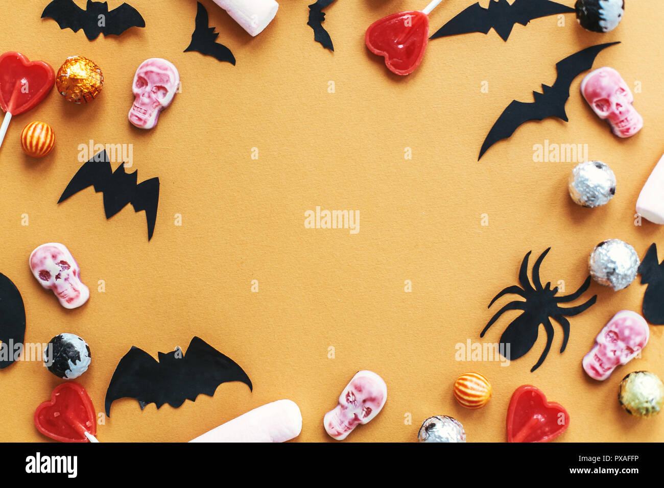 Halloween frame flat lay on orange paper. Holiday candy border with bats, spiders, skulls top view. Trick or treat. Halloween background. Season's gre Stock Photo