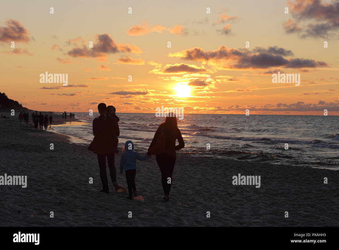 A young family stands on the beach and watches the sunset over the Baltic sea. Stock Photo