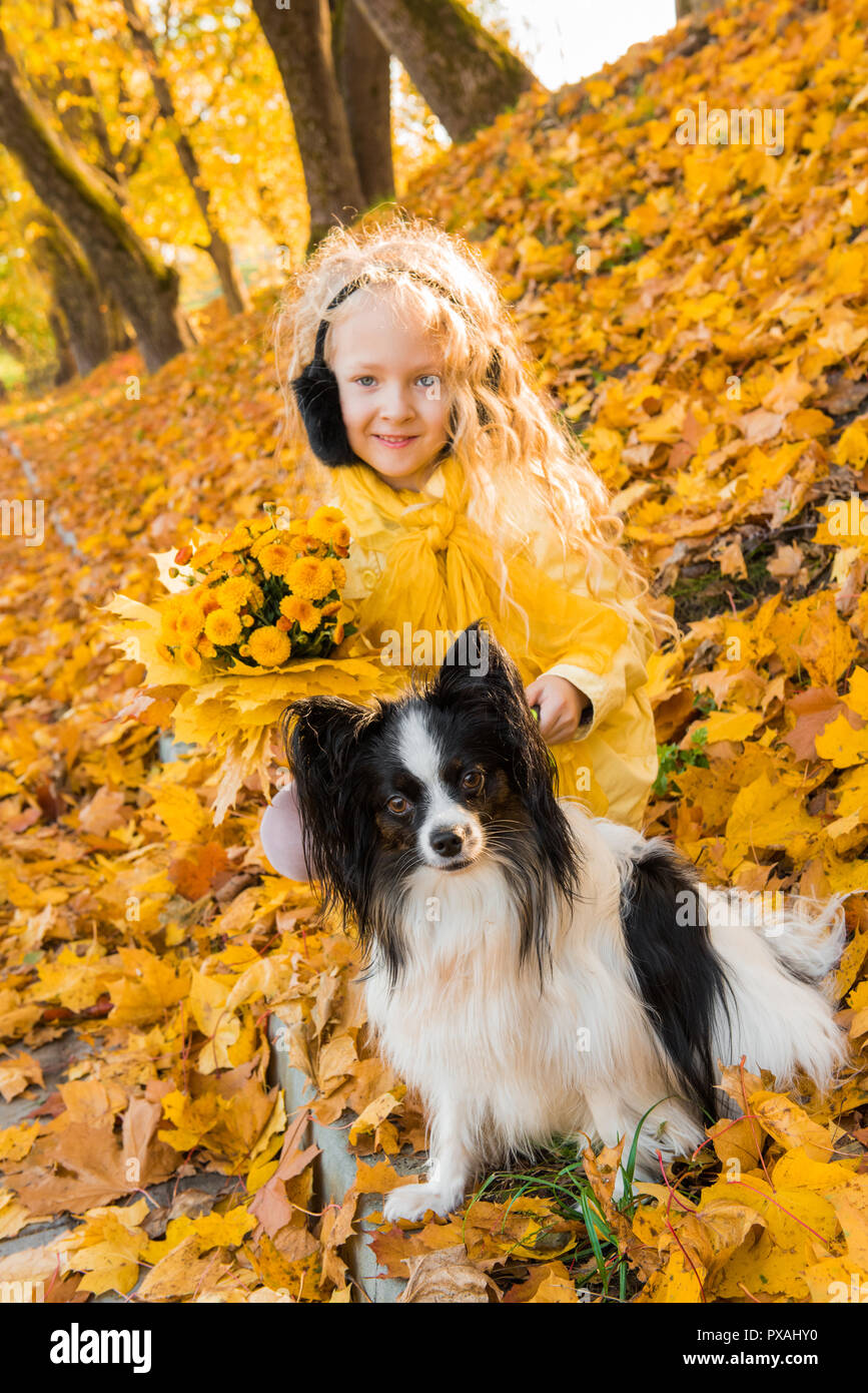 Little beautiful girl with blond hair and small dog in autumn background Stock Photo