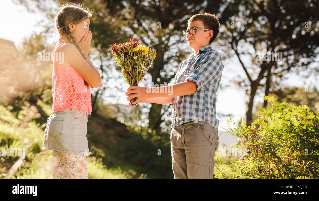 Side view of a boy proposing to his girlfriend with flowers ...