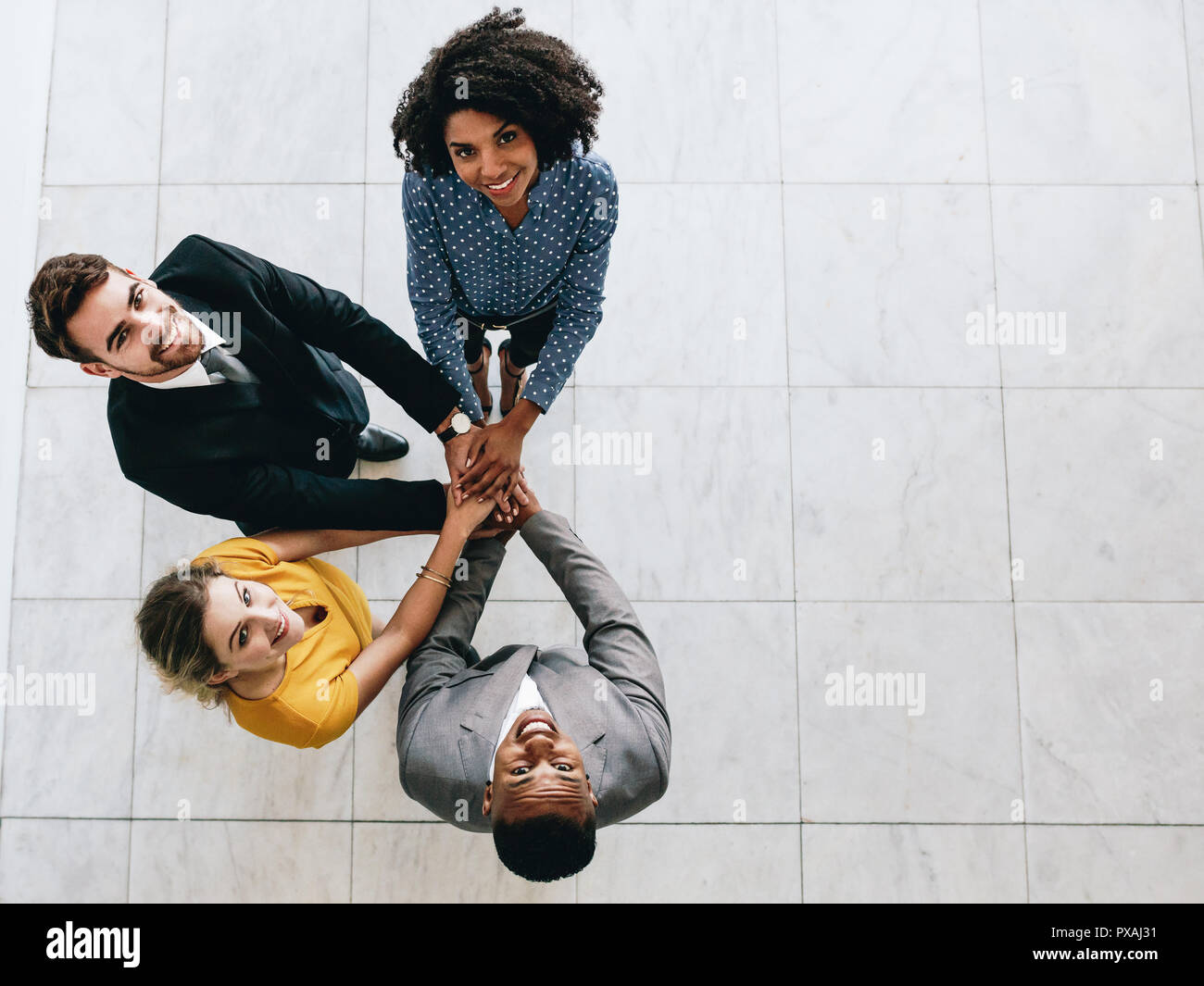 Corporate business professionals putting their hands together and looking up at camera smiling. Multi-ethnic business team with hands stacked together Stock Photo