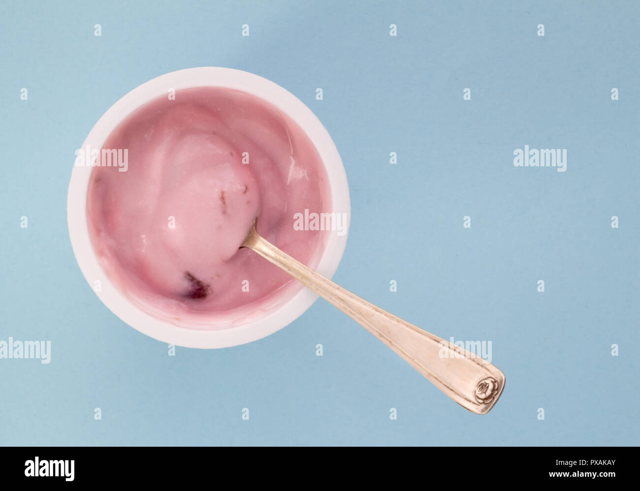 Yogurt in plastic cup close up with small silver spoon, top view photo