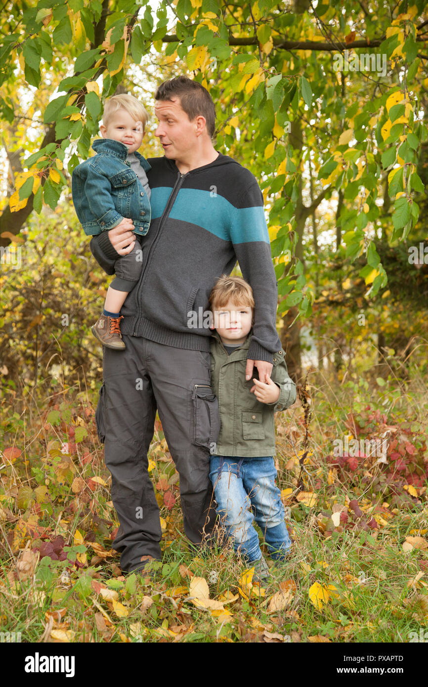 Portrait of family in colorful leaves in autumn woodland. Weather: sunny, dry, white cloud, blue sky. Stock Photo