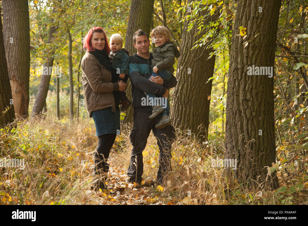 Portrait of family in colorful leaves in autumn woodland. Weather: sunny, dry, white cloud, blue sky. Stock Photo