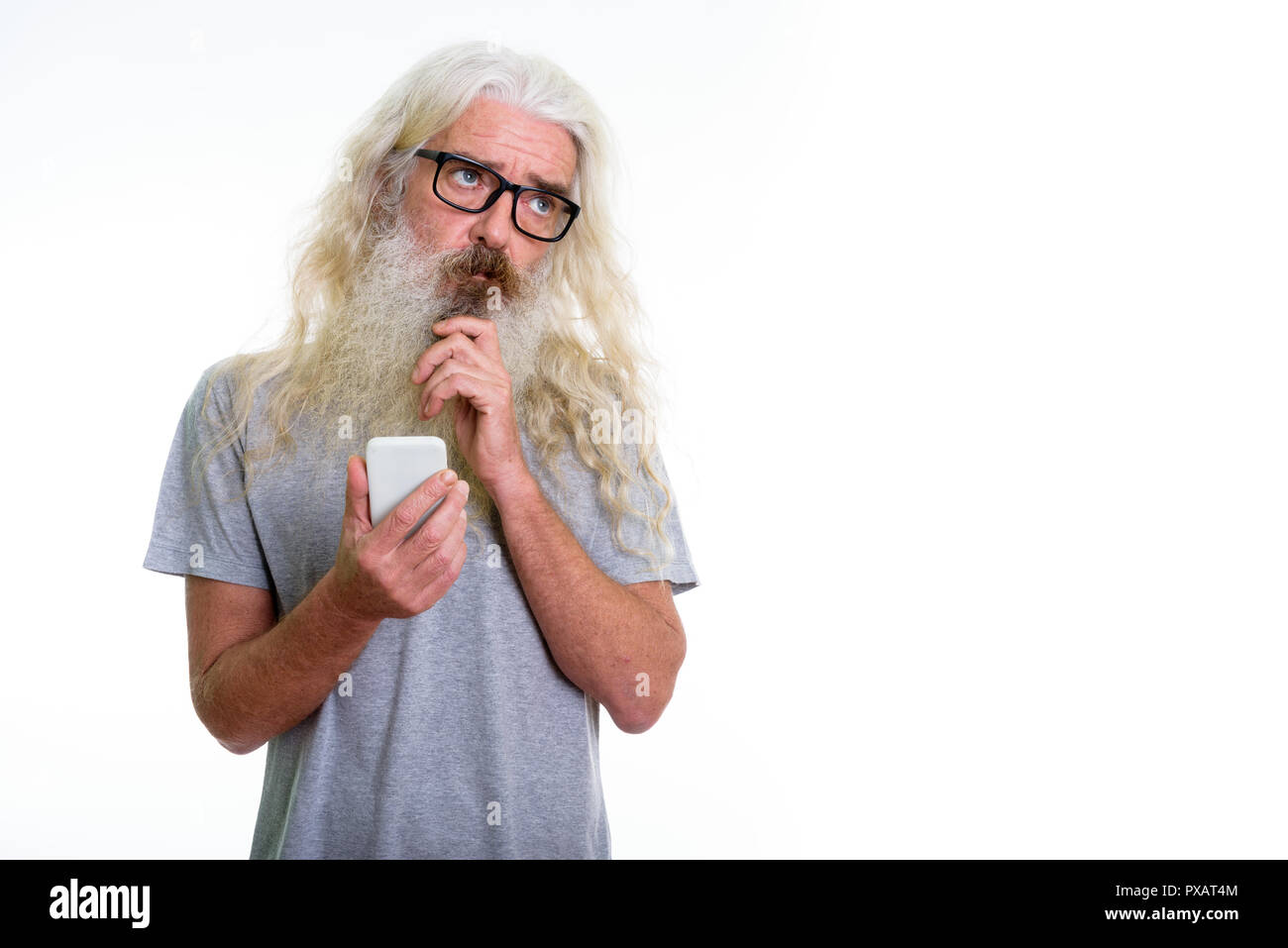 Studio shot of senior bearded man thinking while holding mobile  Stock Photo