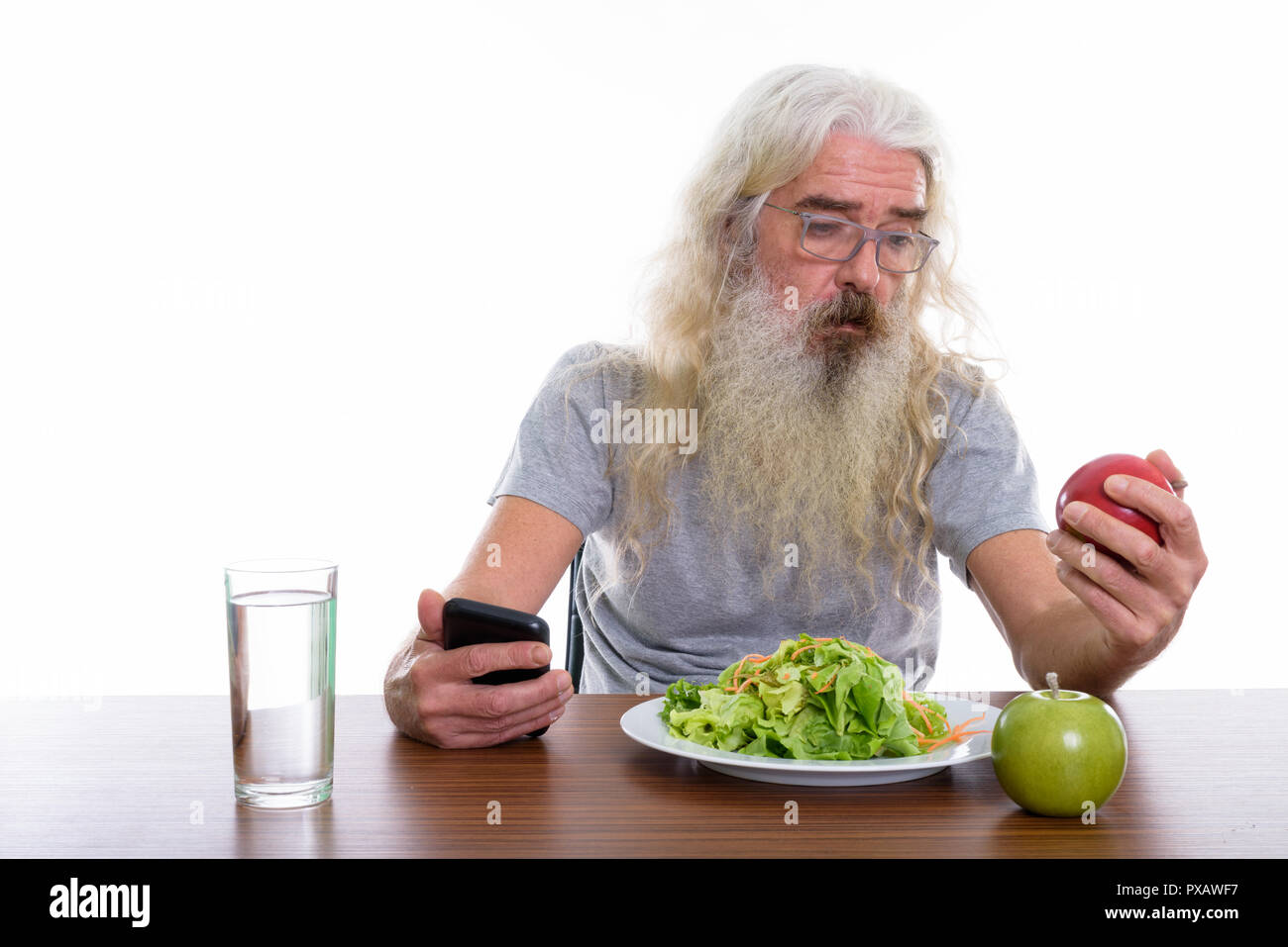 Studio shot of senior bearded man holding mobile phone while loo Stock Photo