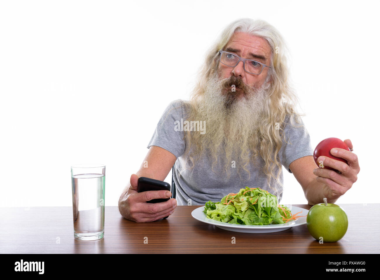 Studio shot of senior bearded man thinking while holding mobile  Stock Photo
