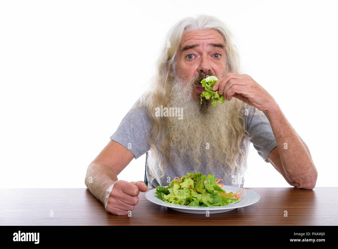 Studio shot of senior bearded man eating plate of salad on woode Stock Photo