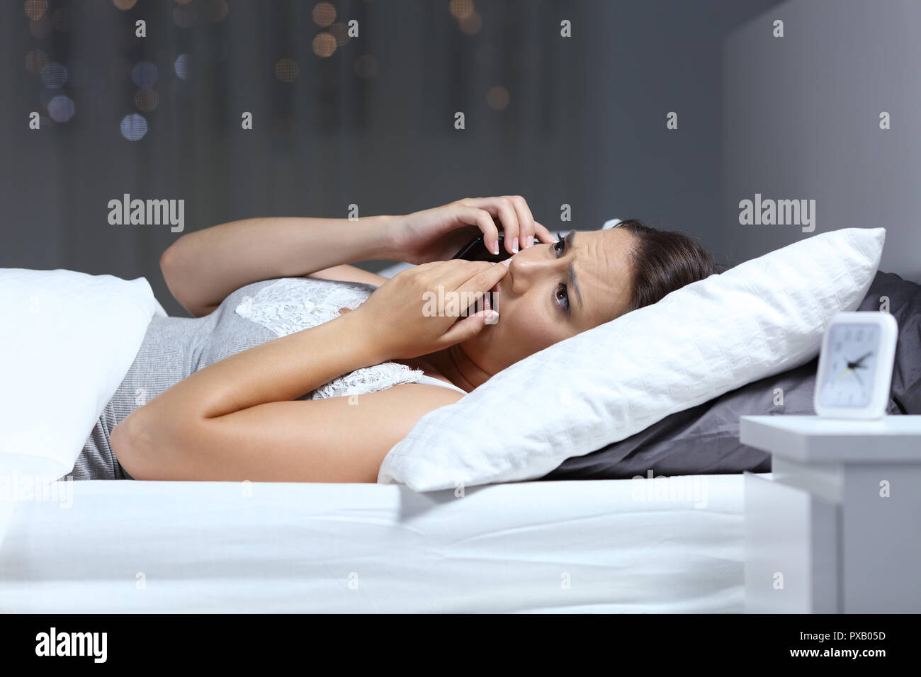 Worried woman receiving a phone call lying on the bed in the night at home Stock Photo