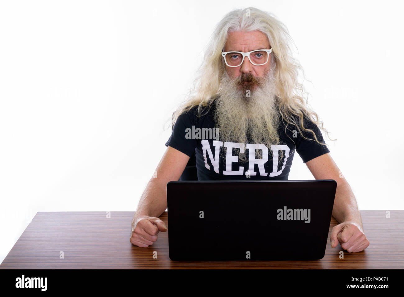 Studio shot of senior bearded nerd man using laptop on wooden ta Stock Photo