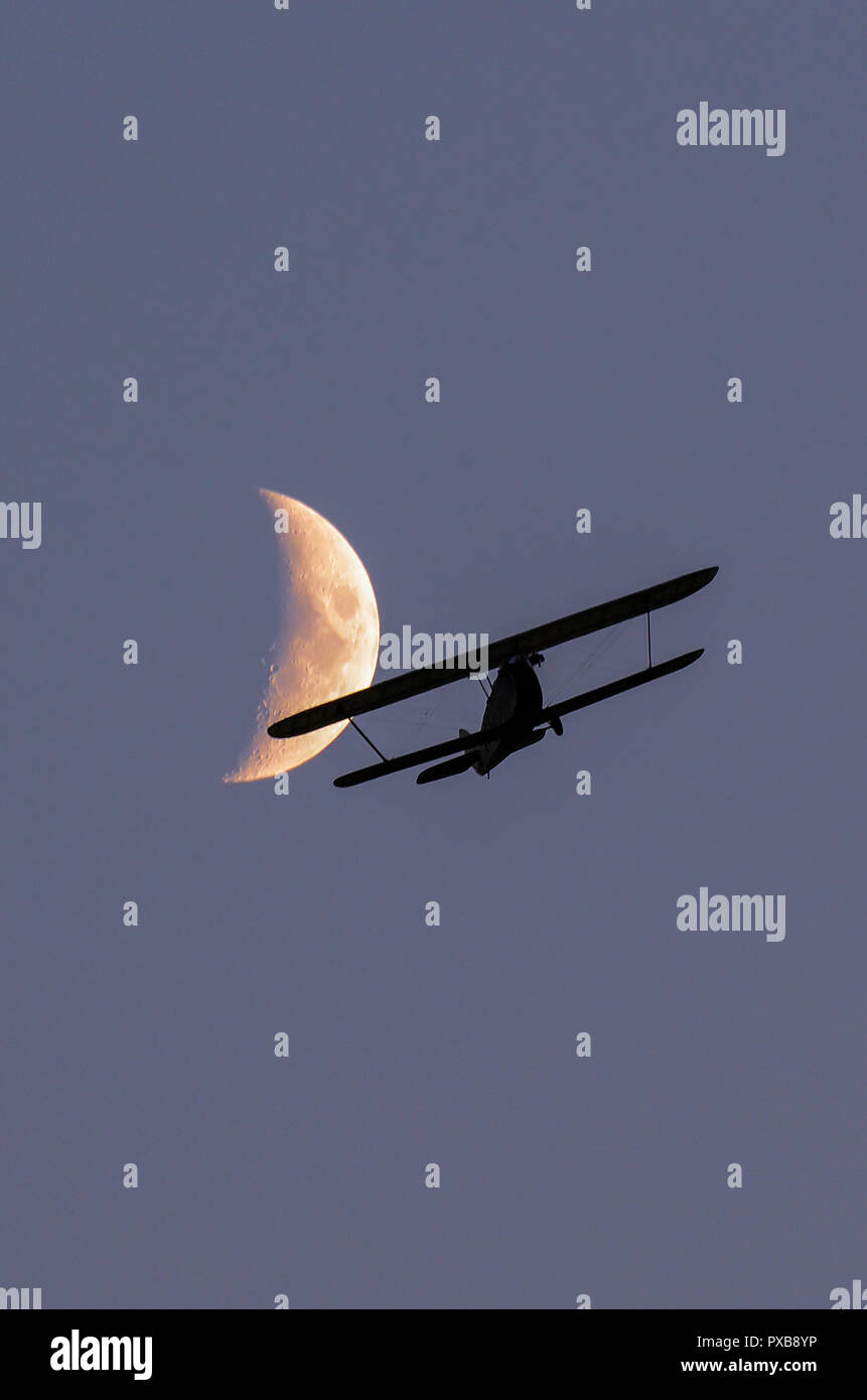 Hawker Cygnet replica vintage biplane flying at dusk with the moon beyond. 1920s biplane ultralight design by Sidney Camm. Light aircraft Stock Photo