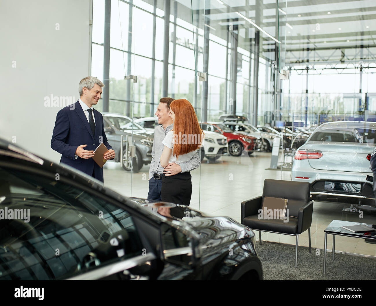 Happy beautiful couple is buying a new car at dealership. Family council Stock Photo