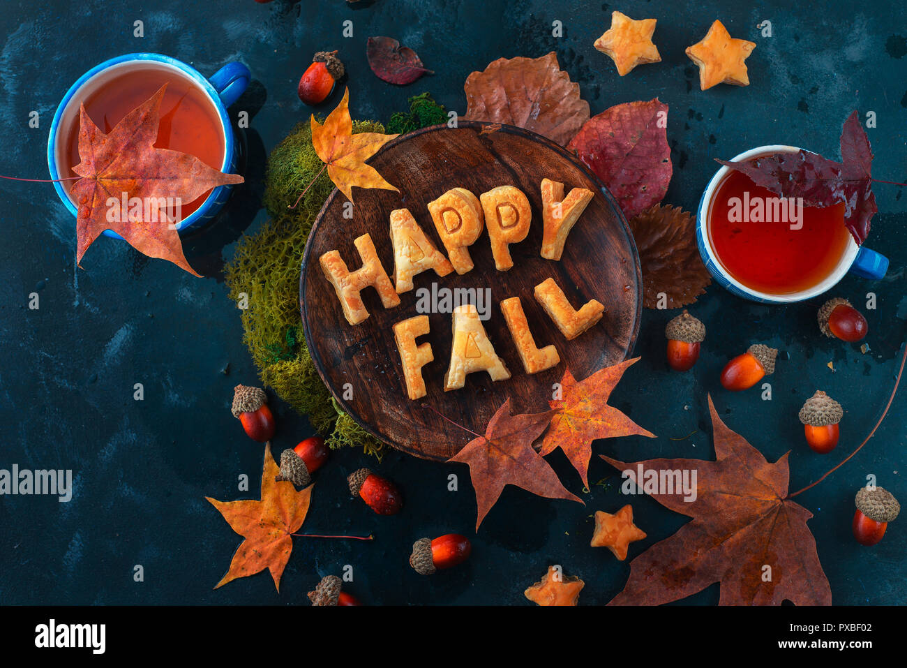 Happy fall food lettering made with cookies. Autumn flat lay with tea, sweets and fallen leaves on a dark background with copy space Stock Photo