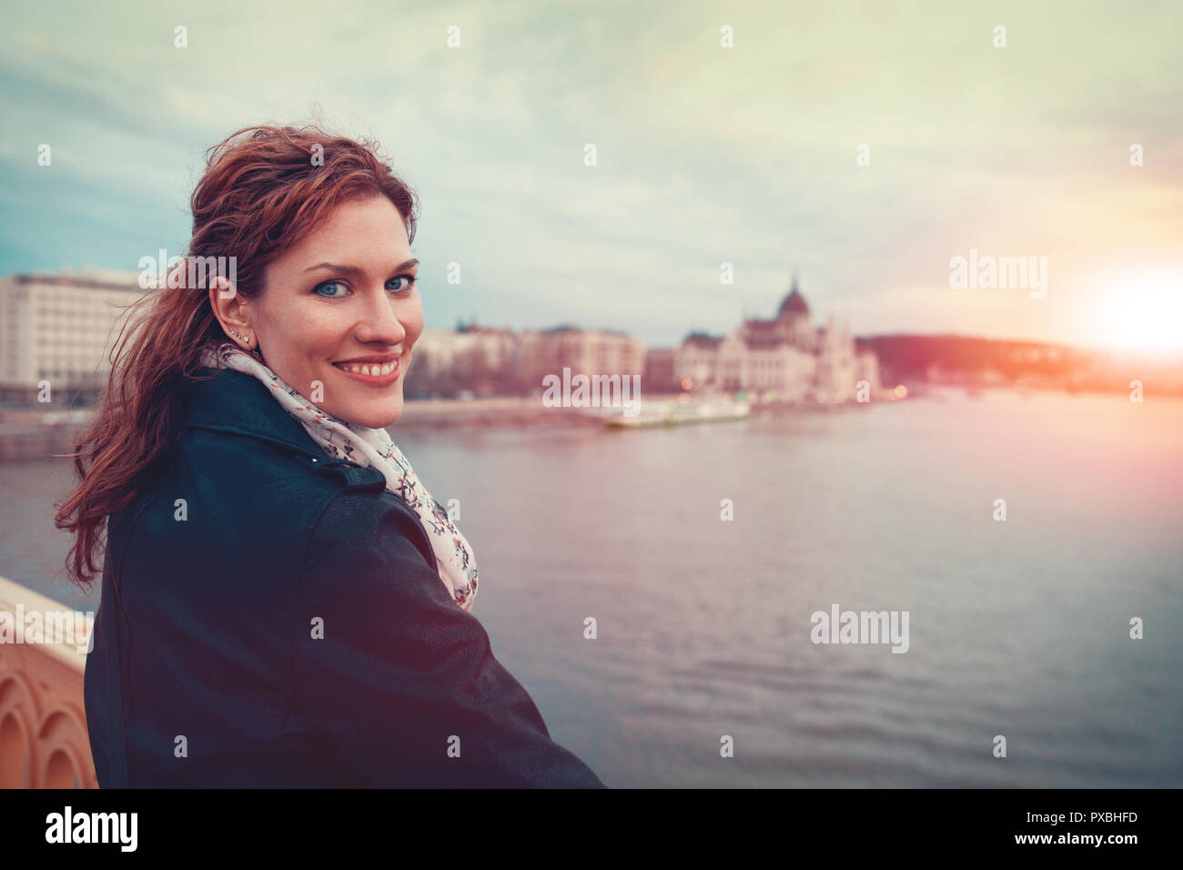 Happy young redhead woman looking back at Budapest cityscape in sunset, smile Stock Photo