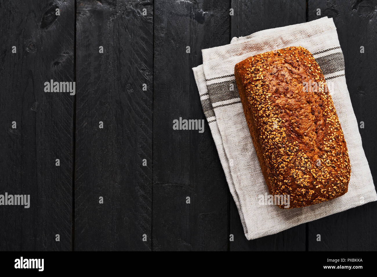 Loaf of whole wheat bread on gray dishtowel over black wooden table. Top view with copy space. Stock Photo