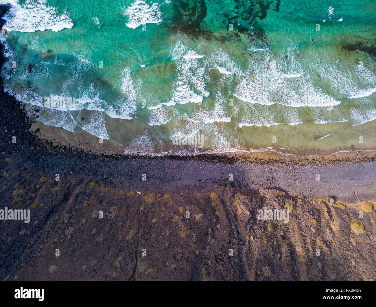 Aerial view of a crystal clear sea with waves and surfers. Playa De La Canteria.Waves crashing on the beach at sunset.Orzola, Lanzarote, Canary Island Stock Photo