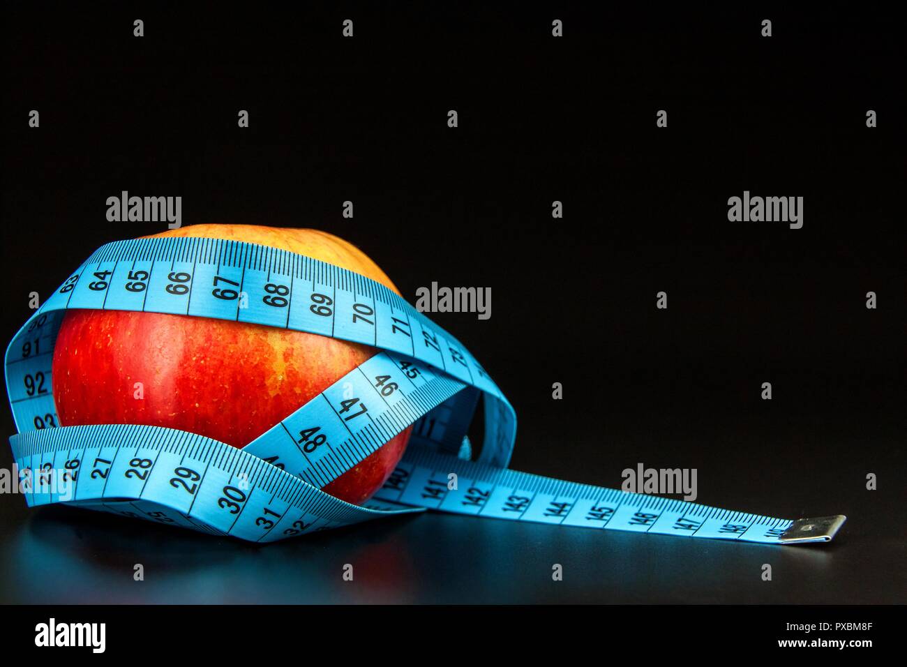 Red apple . Red apple wrapped in a tailor's tape measure on a black background. The concept of weight loss. Healthy diet Stock Photo