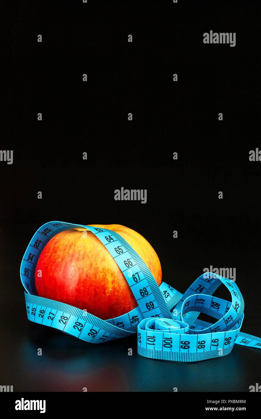 Red apple . Red apple wrapped in a tailor's tape measure on a black background. The concept of weight loss. Healthy diet Stock Photo