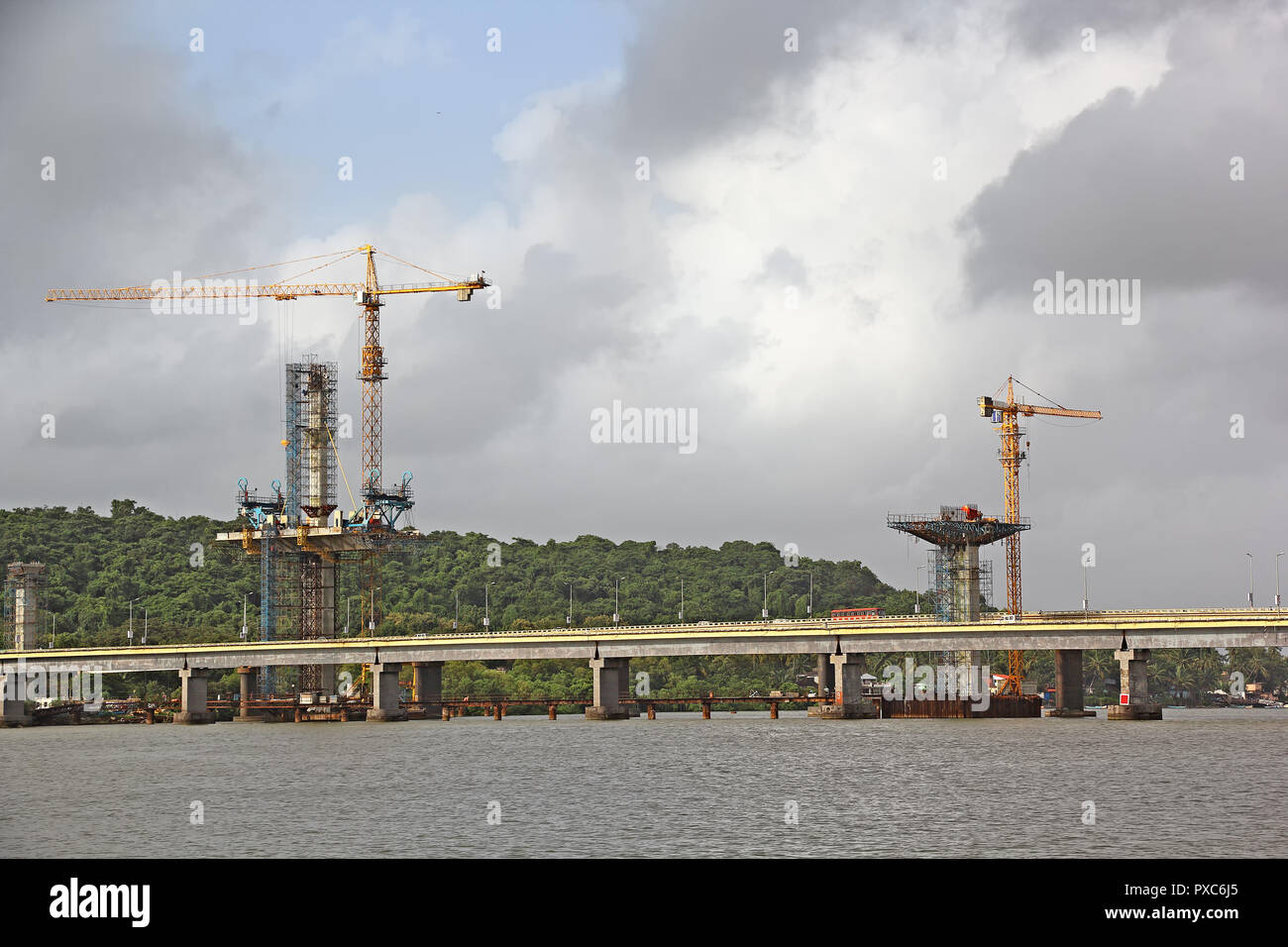 Construction of cable stayed bridge progressing from tall central concrete piers with the aid of tower cranes for the third bridge over Mandovi River Stock Photo