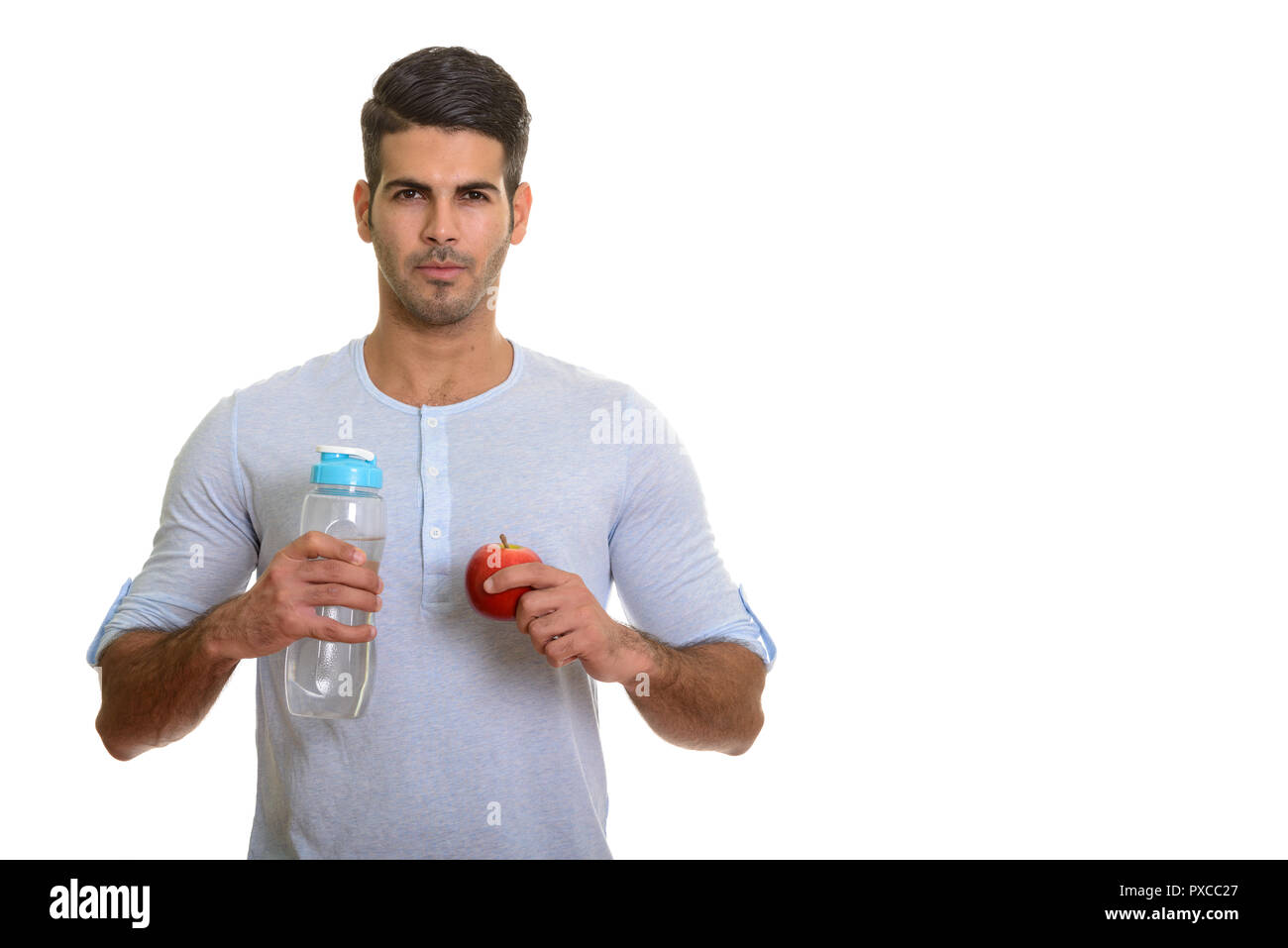 Young handsome Persian man holding water bottle and red apple Stock Photo