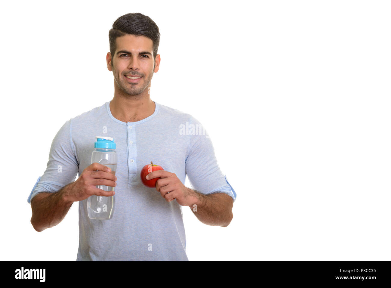 Young happy Persian man smiling and holding water bottle and red Stock Photo