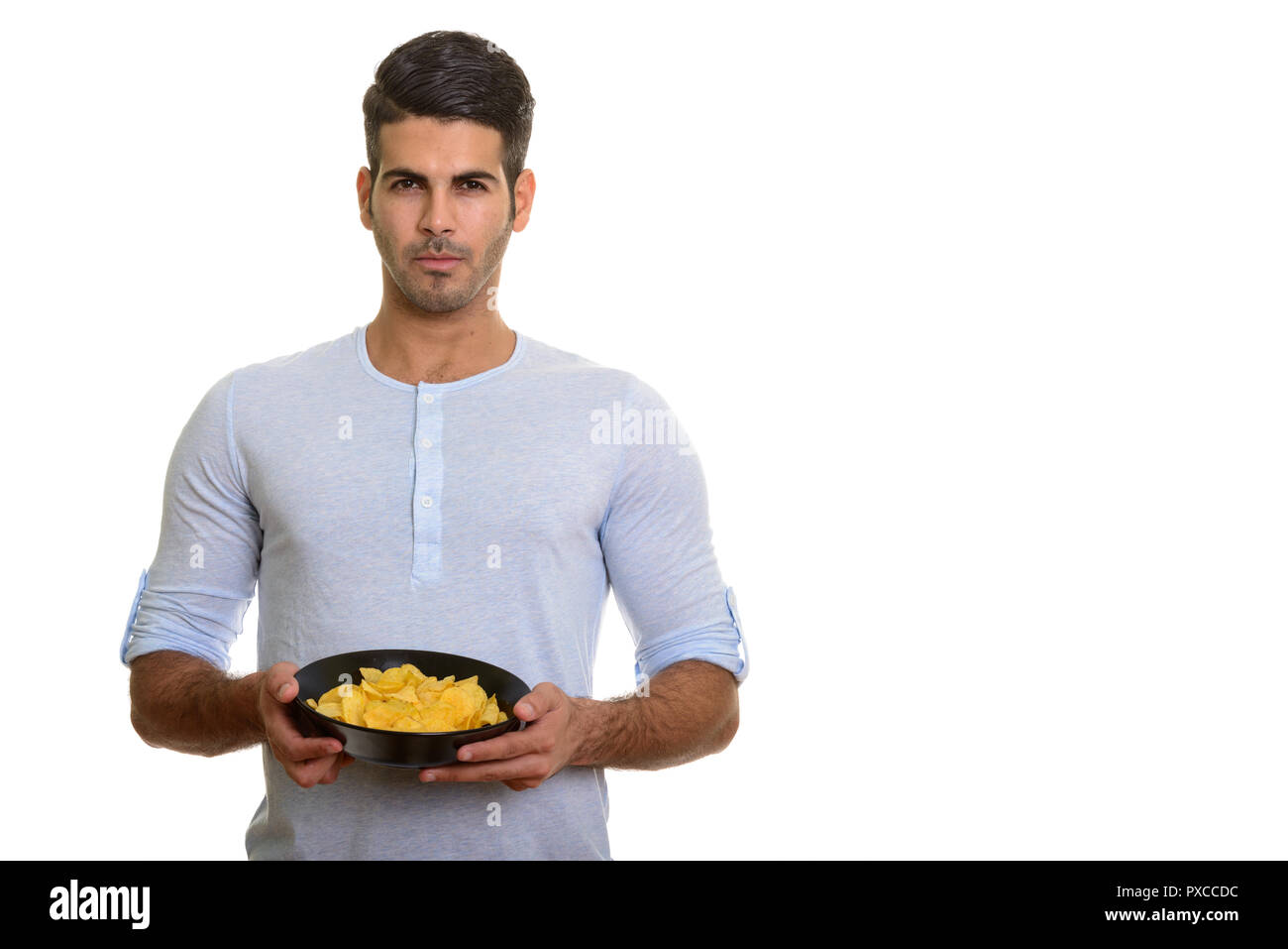 Young handsome Persian man holding bowl of potato chips Stock Photo