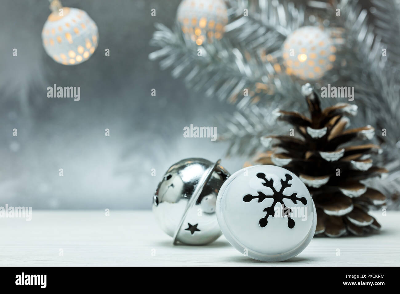 silver pine cone and christmas jingle bells on gray blurred background with fir tree branch and garland lights Stock Photo