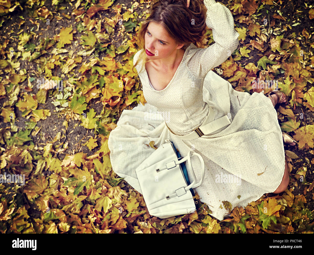 Autumn fashion dress woman sitting fall leaves city park outdoor. Stock Photo