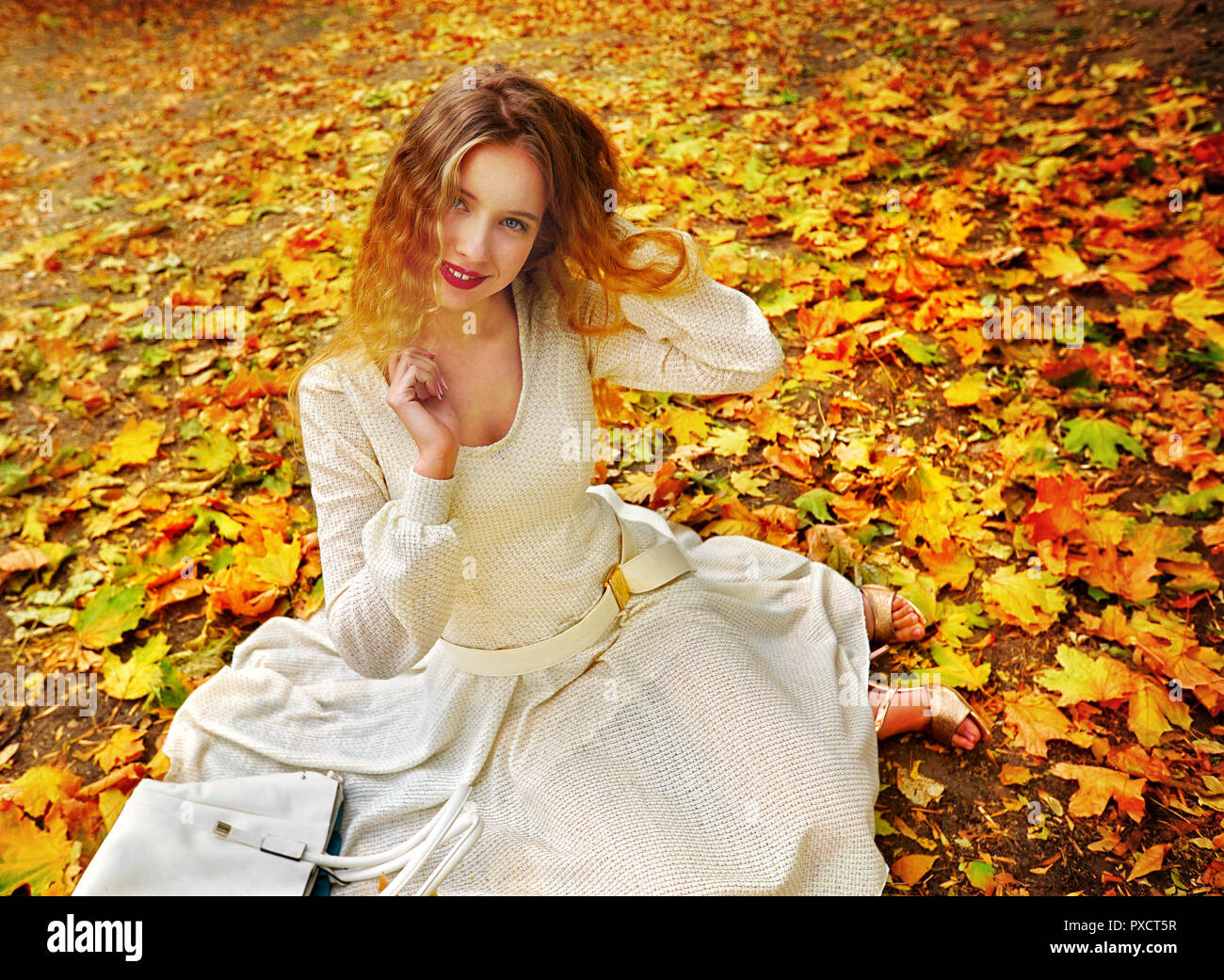 Autumn fashion dress woman sitting fall leaves city park outdoor. Stock Photo