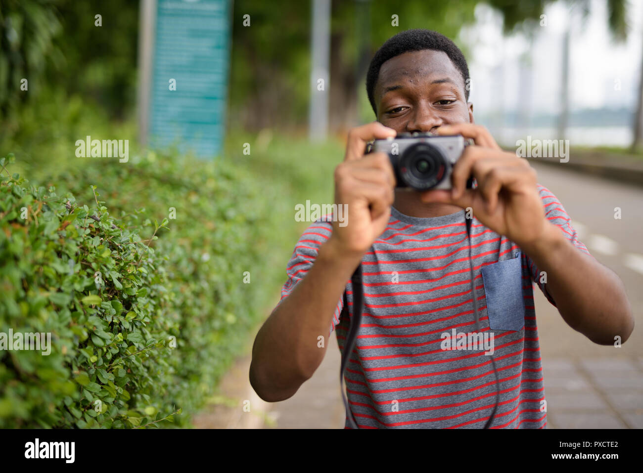 Young handsome African man taking pictures with camera in park Stock Photo