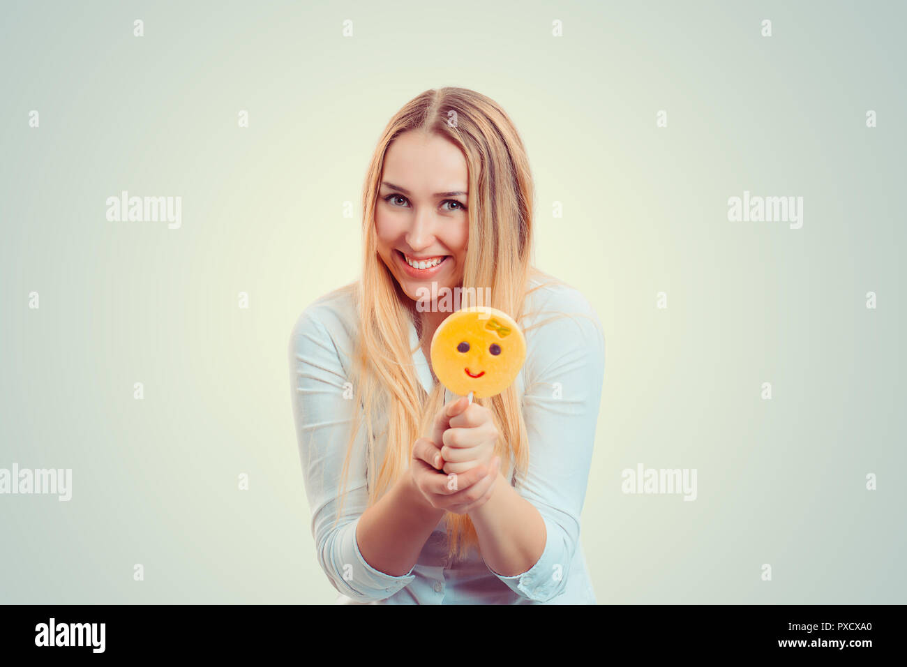 Bright blond woman holding stick with emoji lollipop smiling at camera Stock Photo