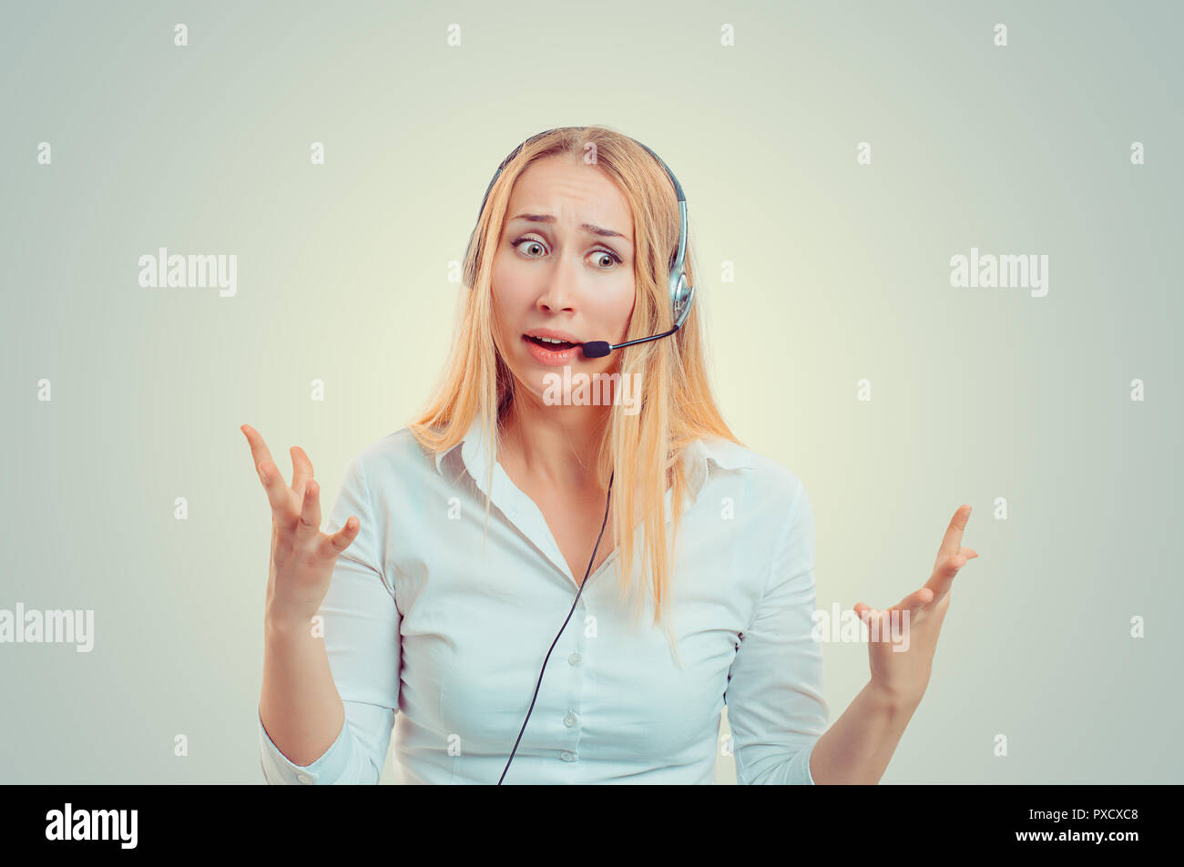 Young blond woman in white shirt wearing headset in puzzlement and gesturing in helplessness Stock Photo