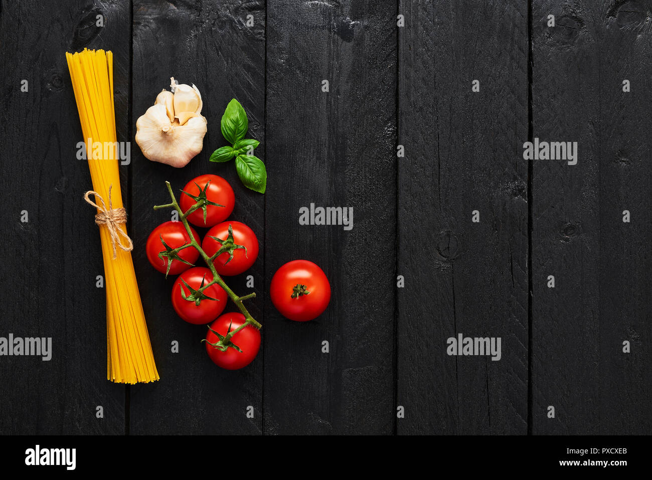 Food background for tasty Italian dishes with spaghetti, tomato garlic and basil. Various cooking ingredients on black wooden table. Top view with cop Stock Photo