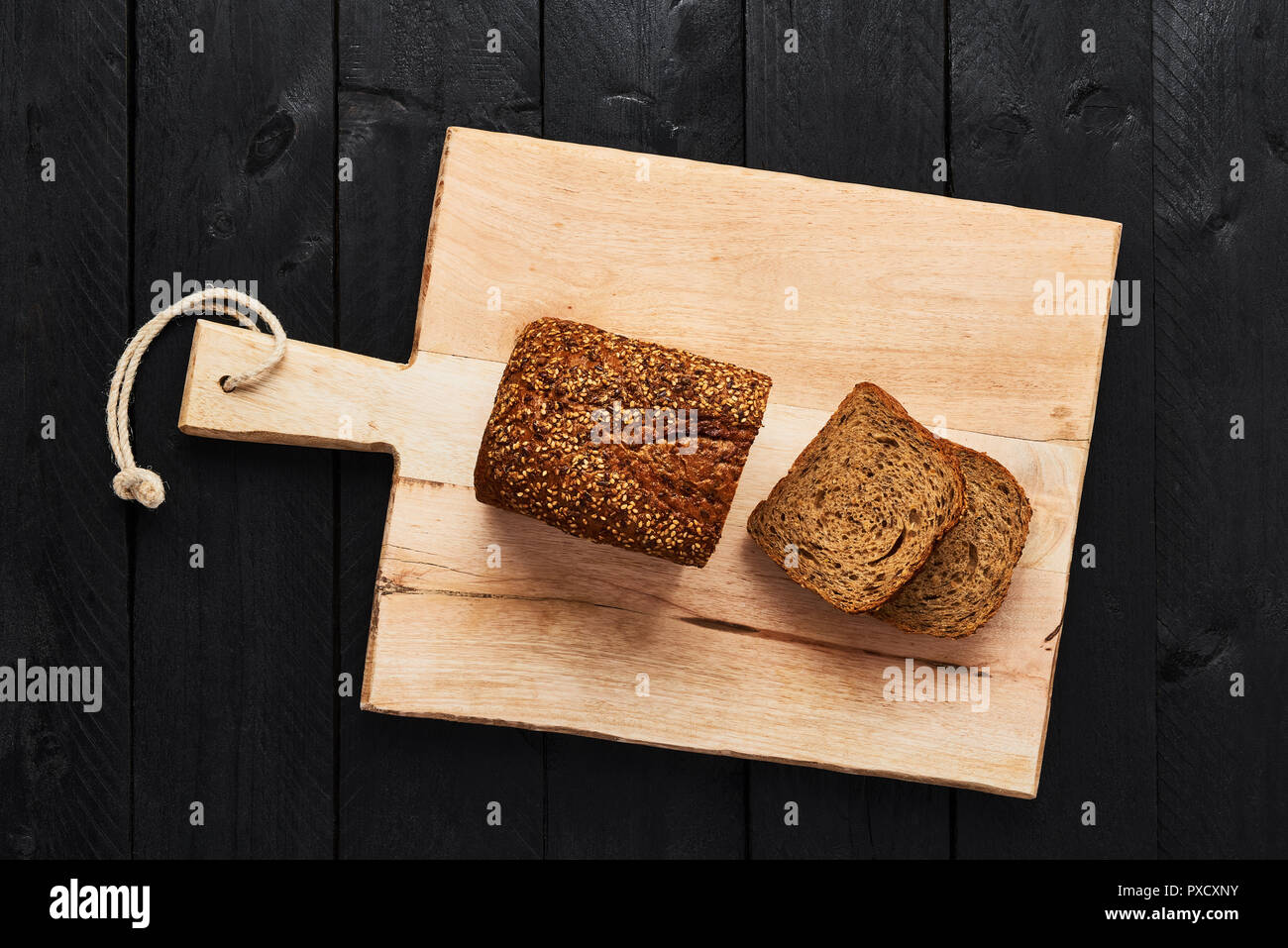 Loaf of sliced whole wheat bread on cutting board over black wooden table. Top view. Stock Photo