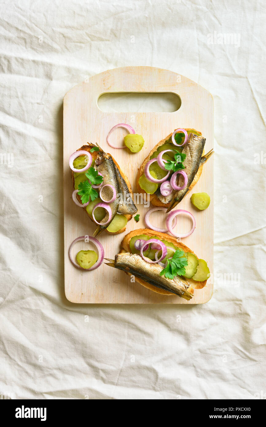 Sandwiches with sprats, marinated cucumber and onion on wooden board. Top view, flat lay Stock Photo