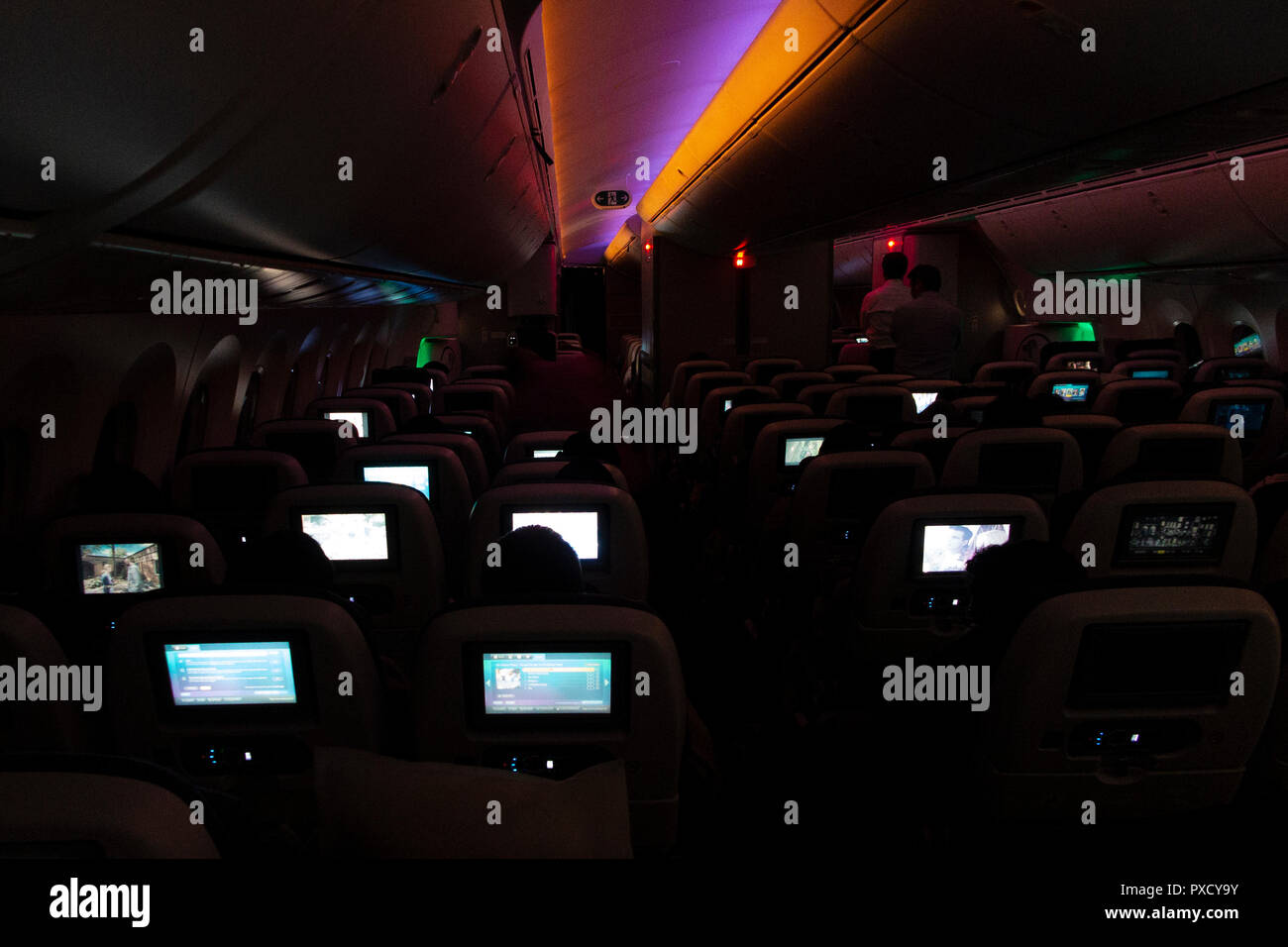 Video screens light up the interior of a long haul flight on a BA777 at night Stock Photo
