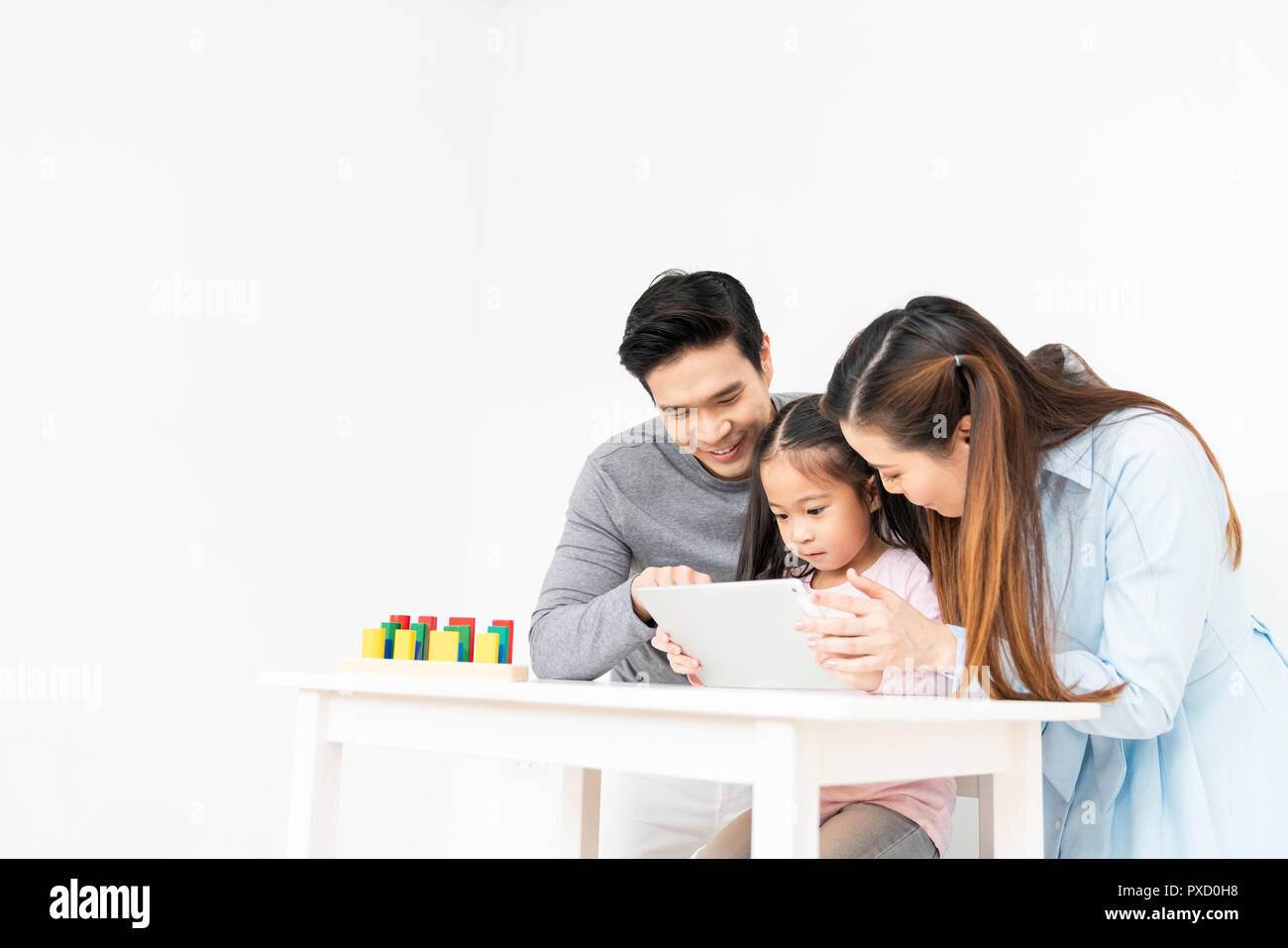 Young lovely Asian family, parents and small kid using digital tablet at home with copy space. Father and mother teaching little girl daughter Stock Photo
