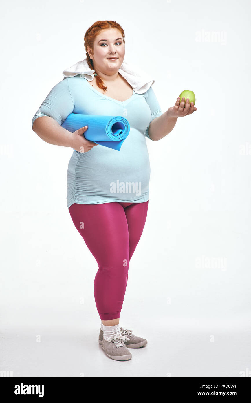 Funny picture of amusing, red haired, chubby woman on white background. Woman holding a mat. Stock Photo