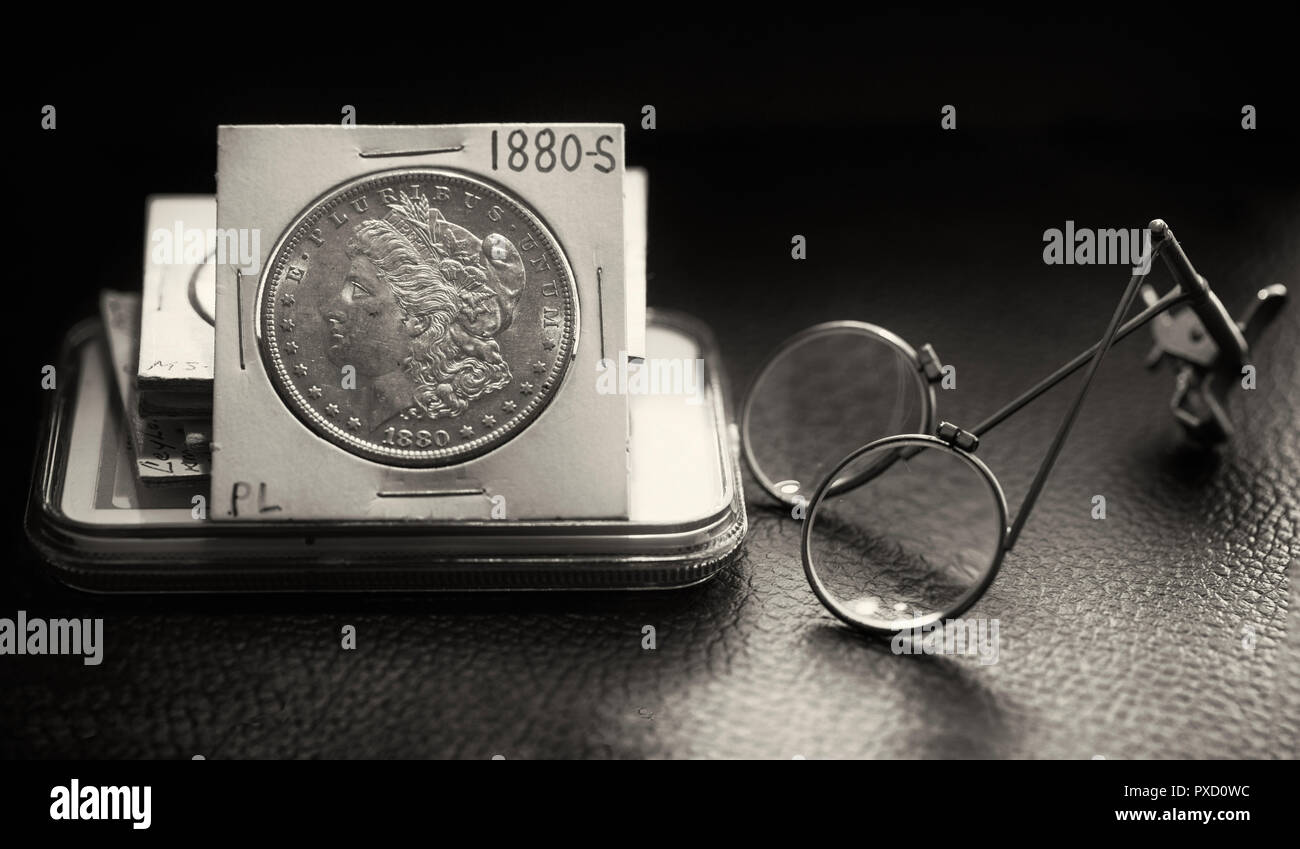 Coin Collector Desk with stack of coins featuring a beautiful mint state Morgan Dollar and magnifier glass in black and white Stock Photo