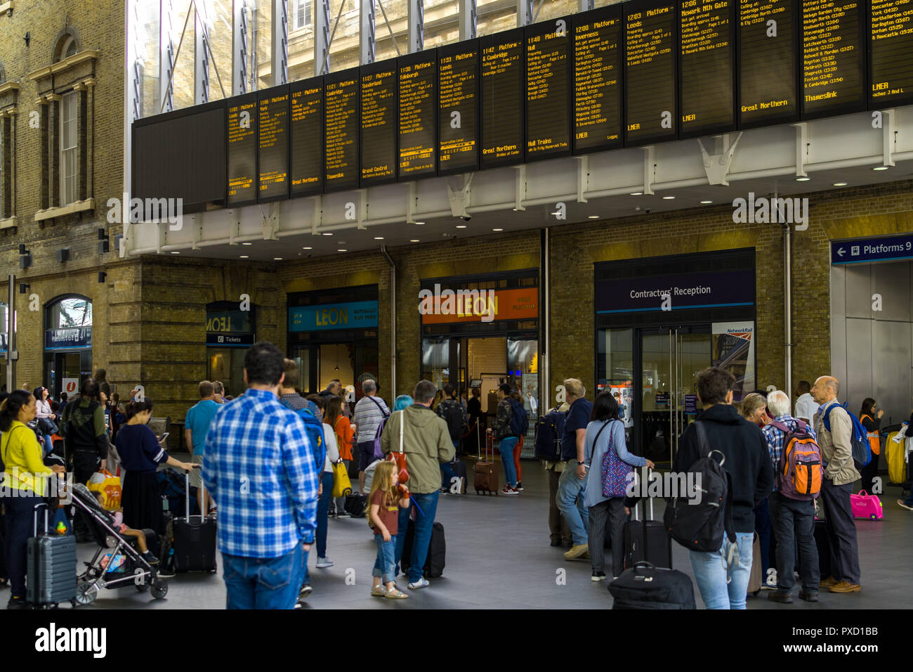 Commuters standing looking at the main electronic train noticeboards in the concourse of King's Cross station, London, UK Stock Photo