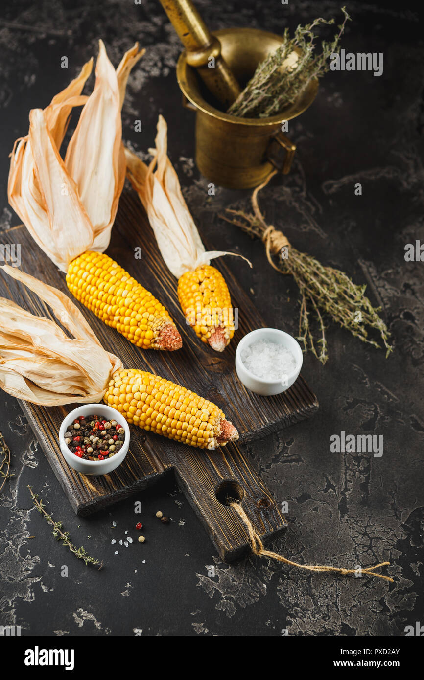 Yellow corn on cobs on grunge dark table, with Thyme, salt and pepper, closeup Stock Photo