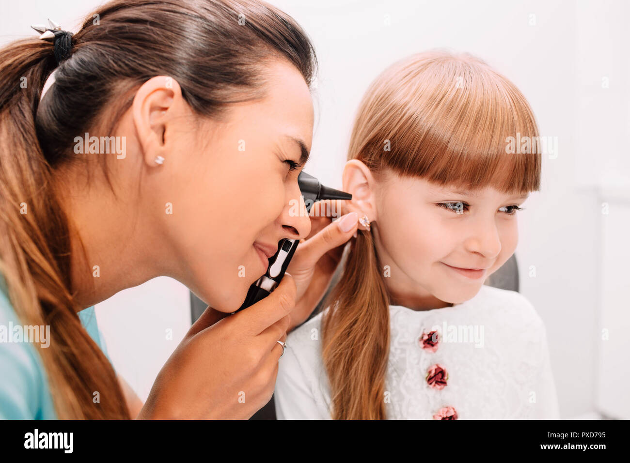 Smiling doctor examining child ear using Otoscope Stock Photo