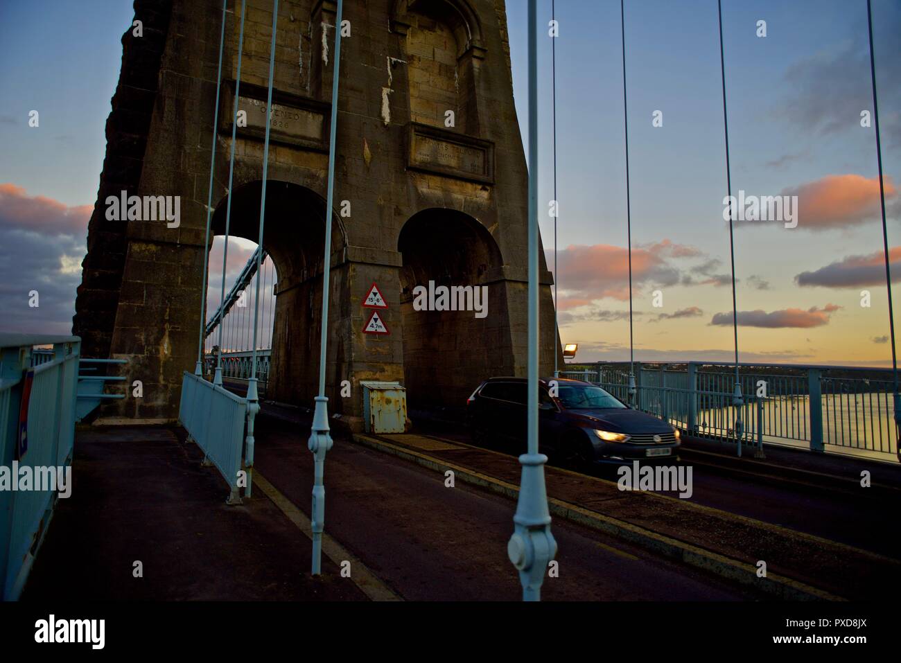 A car crosses the Menai Suspension Bridge at dawn, Bangor, Wales, UK Stock Photo