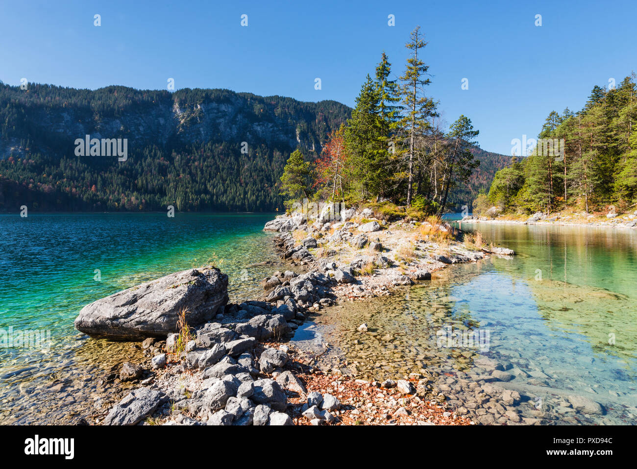 Stones on the shore of the headland over to island Braxeninsel in the Lake Eibsee surrounded by autumn forest, Bavaria, Germany Stock Photo