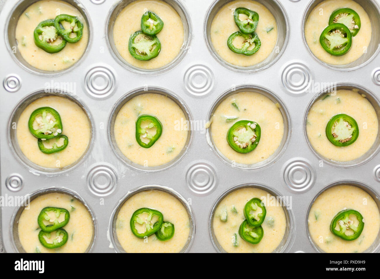 Flat lay. Cornbread batter in muffin pans garnished with jalapeno