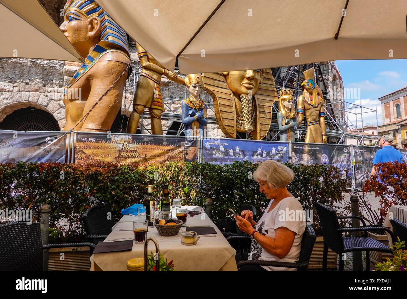 Verona, Italy. Femal tourist waiting for her food in a small restaurant at the Colosseum, watchd by colossal statues for the Aida-Performa Stock Photo