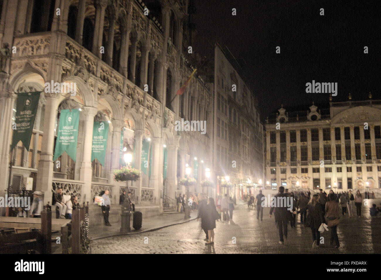 View of the Grande Place, in Brussels, Belgium at night. Elegant Gothic buildings line the historic square, as sightseers pass by. Stock Photo