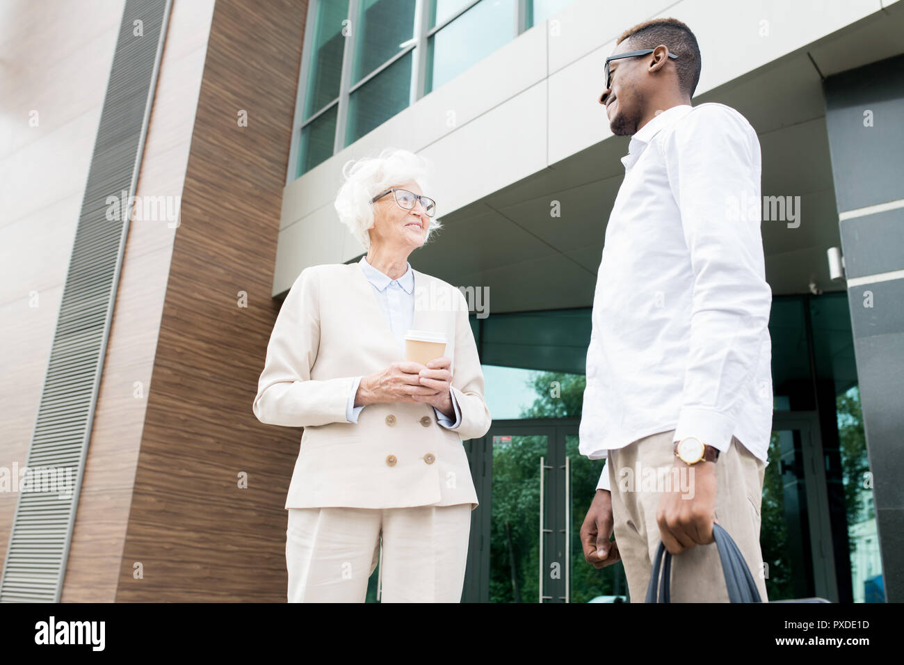 Smiling successful senior lady talking to colleague outdoors Stock Photo